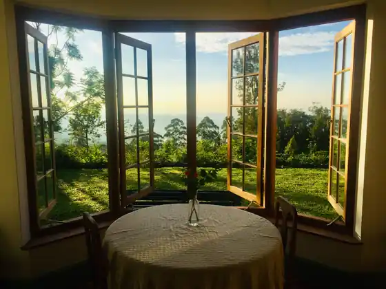 A table laid in the bungalow bay window, windows open onto the garden and hills