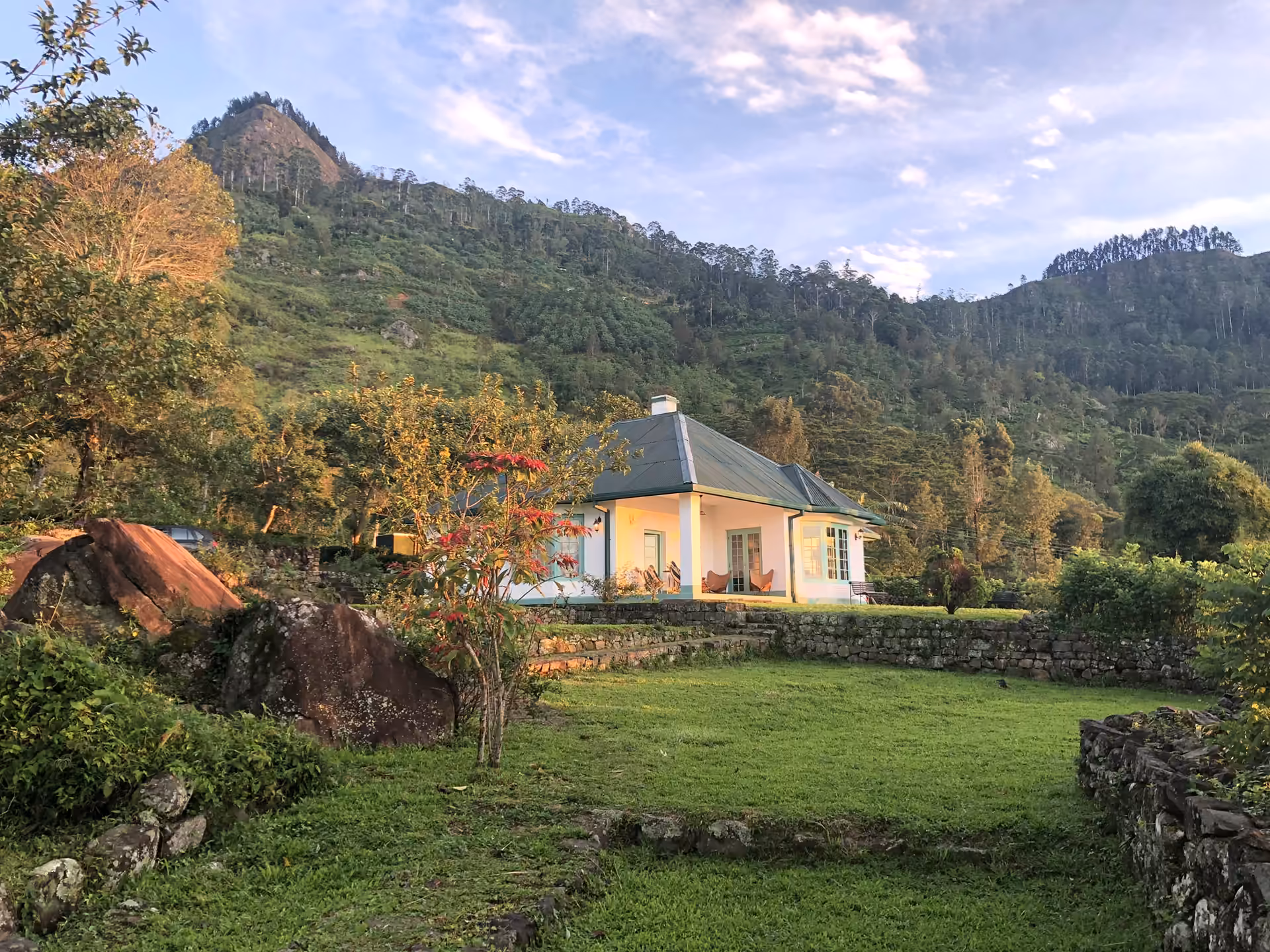 Haldummulla Estate's white planter's bungalow on its lawn beneath forested hills in late afternoon light