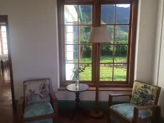 Armchairs in the sunny bungalow sitting room by tall windows onto the garden