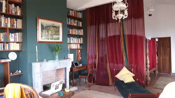 The Library Suite's book-lined sitting room opening onto the four-poster bed behind deep red curtains