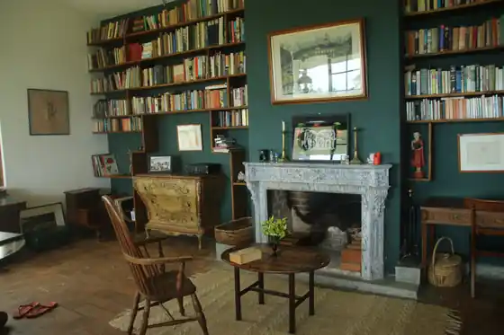 The Library Suite's sitting room: dark green walls, floor-to-ceiling bookshelves, a grey marble fireplace and a Windsor chair