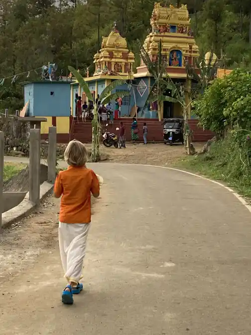 A child walking towards a brightly painted Hindu temple in the village